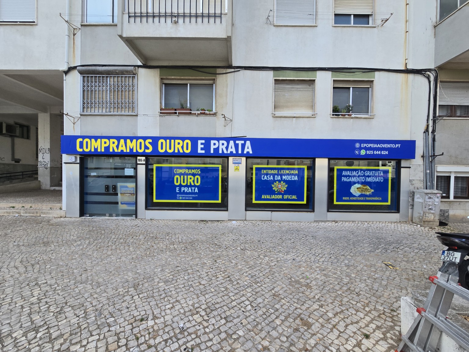 Fachada de loja de compra de ouro e prata com letreiro azul e decoração de montras em azul e amarelo, trabalho da CIM